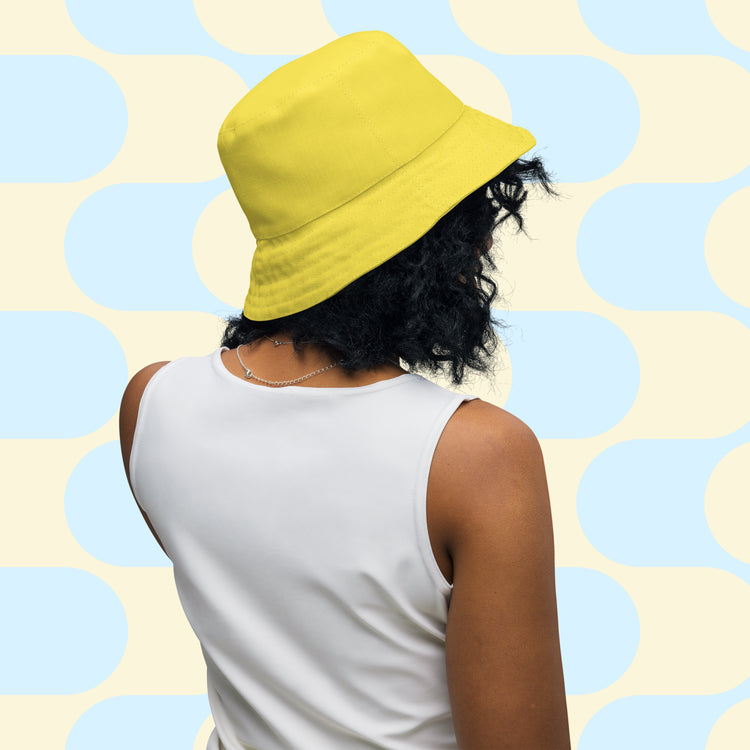 A person with curly hair wears the Bloomscape Reversible Bucket Hat by My Favourite Colour is Rainbow, paired with a sleeveless white top. 