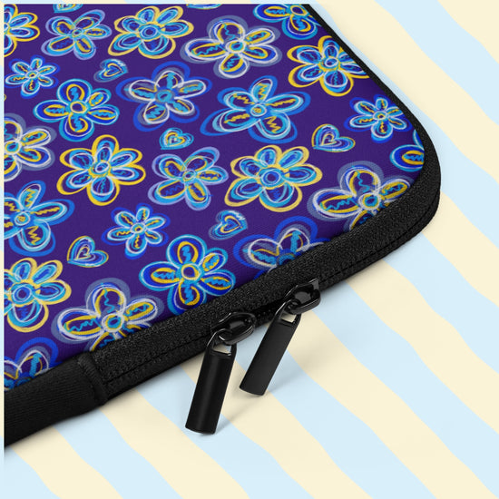 A close-up of the Bloomscape Laptop Sleeve by My Favourite Colour is Rainbow: A water-resistant case with black zippers, featuring a vibrant design of blue and yellow flowers and hearts on a royal blue background. It has two zips and black padded zipper binding.  The print is only on one side; the other side is black.