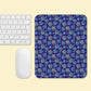 A white keyboard and mouse sit on a light yellow surface. To the right, theres a Bloomscape Mouse Pad by My Favourite Colour is Rainbow, featuring a colorful floral pattern on a dark blue background.