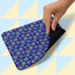 A hand holds the Bloomscape Mouse Pad by My Favourite Colour is Rainbow, showcasing a blue floral pattern with yellow and red accents on one side and black on the other, set against a backdrop of light blue and pale yellow diagonal squares.