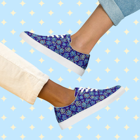 Two individuals wearing 'Bloomscape' Canvas Sneakers by My Favourite Colour is Rainbow: one in light pants, the other in rolled-up jeans. The shoes feature a design of large flowers and small hearts in shades of blue and yellow on a royal blue background.