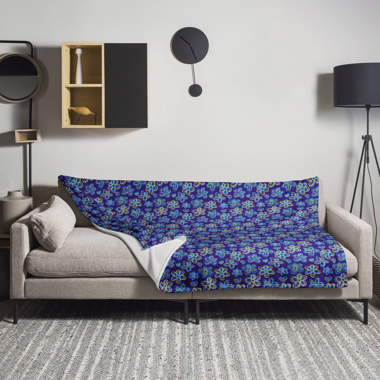 A cosy living room has a light grey couch draped with the Bloomscape Throw Blanket by My Favourite Colour is Rainbow.   A modern clock hangs above, a black floor lamp is on the right, and a decorative wall shelf with vases and a small sculpture is on the left.