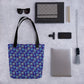 Flat lay on a speckled surface featuring the Bloomscape Tote Bag by My Favourite Colour is Rainbow. Accompanied by sunglasses, notebooks, pens, a phone, a camera clip, a gray tassel keychain, and a laptop.