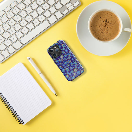 A white keyboard, the MagSafe® compatible Bloomscape iPhone Case by My Favourite Colour is Rainbow with a floral design, a notebook with a pen, and a cup of coffee sit on a bright yellow surface.