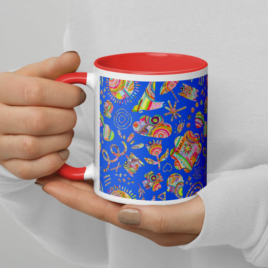 A person holds the Blue Summer Sorbet Mug by My Favourite Colour is Rainbow, featuring vibrant abstract fish against blue, with a contrasting red interior and handle. Dressed in a white top with manicured nails, they embody the perfect summer escape.