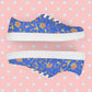 My Favourite Colour is Rainbow's Blue Summer Sorbet Canvas Sneakers feature cut outs of my Summer Sorbet print in a fun mix of suns, rainbows, ice creams and other abstract shapes, set against a striking blue backdrop.  The shoes have white soles and laces, offering an ideal mix of style and comfort.  Shown on a pastel pink background with white diamond accents