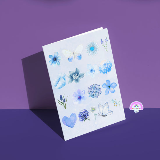 The Blue Watercolour Greeting Card by My Store enchants with butterflies amid blue flowers and heart designs on a shadowed purple background, featuring a small rainbow logo in the lower right corner.