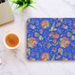 The Blue Summer Sorbet Mouse Pad by My Favourite Colour is Rainbow features a colorful abstract tribal pattern with geometric shapes and swirls in pink, yellow, and green. Its on a marble surface next to coffee, part of a laptop, and a small plant.