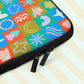 A close-up of the Colour Block Laptop Sleeve by My Favourite Colour is Rainbow, featuring a grid of abstract shapes in colours with a vintage vibe.  It has a double black zipper and padded zipper binding.  It is shown on a pastel background.  The print is on only one side of the laptop sleeve, the other side is black.
