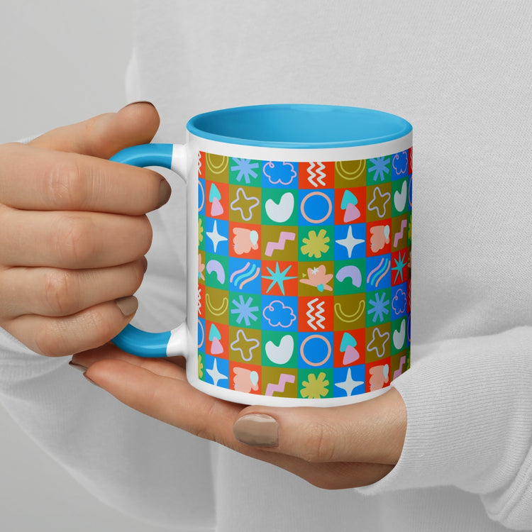 Hands display the vibrant hues of My Favourite Colour is Rainbows Colour Block Mug, a white mug with a blue interior and a geometric design filled with hearts, stars, and abstract symbols in red, blue, green, and orange.