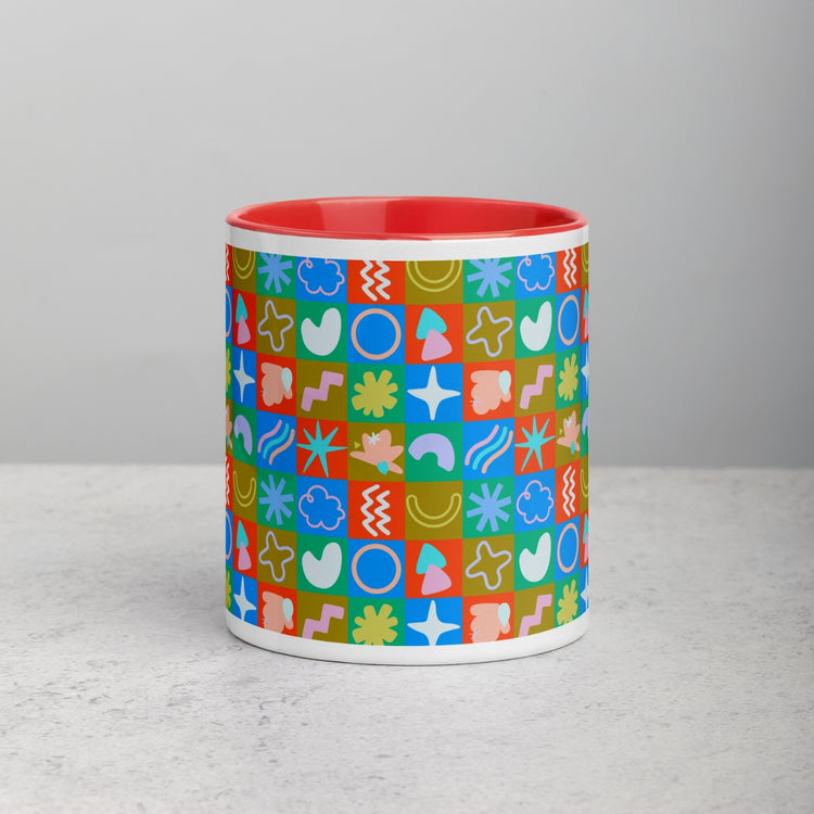 The Colour Block Mug by My Favourite Colour is Rainbow features a red interior with a geometric design in blue, green, red, and orange. It rests on a light gray surface against a plain gray background, highlighting its vivid mix of colors and patterns.