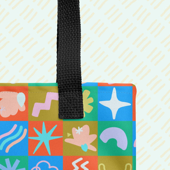 A close-up of the Colour Block Tote Bag by My Favourite Colour is Rainbow. Its a spacious tote with sturdy black handles, featuring vibrant patchwork with abstract shapes in bright orange, green, and blue hues.