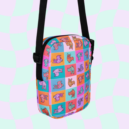 The Crazi Corgis Mini Crossbody Bag by My Favourite Colour is Rainbow has a vibrant checkerboard of pink, orange, and blue squares with beanie baby-style bears. It features an adjustable black strap and zipper set against wavy pastel stripes and is water-resistant.