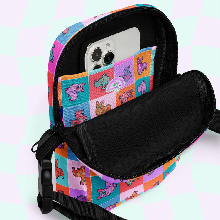 The Crazi Corgis Mini Crossbody Bag by My Favourite Colour is Rainbow features a vibrant patchwork design with cartoon bears and adjustable straps. Inside the sturdy bag, an open pocket reveals a smartphone with three camera lenses on a pastel checkered background.