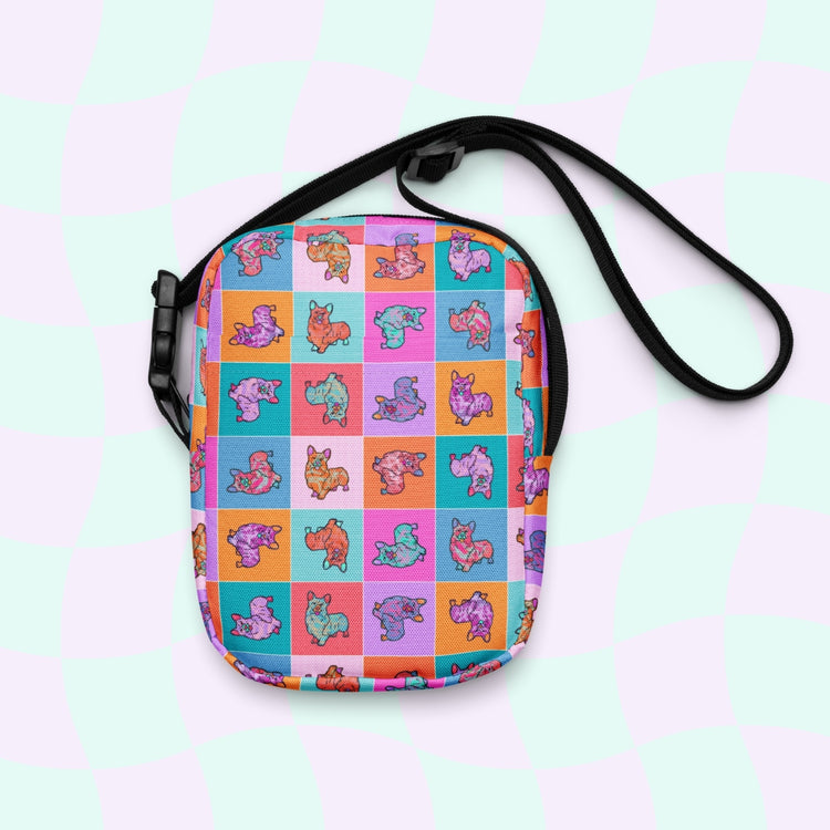 The Crazi Corgis Mini Crossbody Bag by My Favourite Colour is Rainbow showcases a colorful cartoon corgi pattern on a pastel checkered background. This sturdy, water-resistant bag features adjustable straps for convenient carrying.