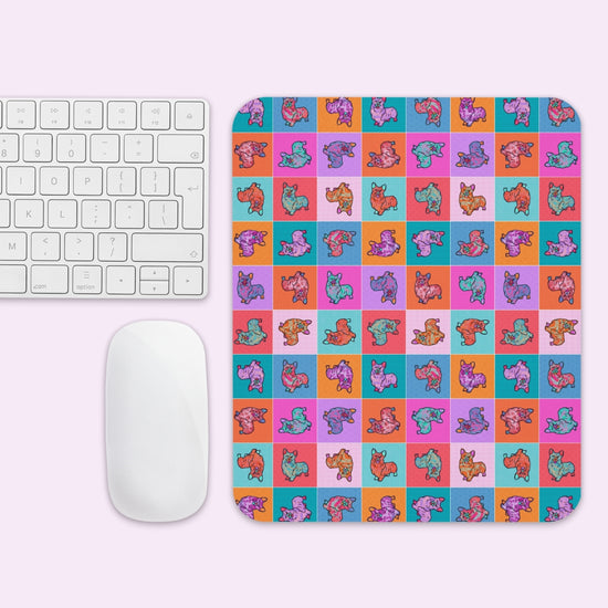 The Crazi Corgi Mouse Pad by My Favourite Colour is Rainbow features cartoon animals in various poses and colors on a checkered background, placed beside a white keyboard and mouse on a light pink surface.