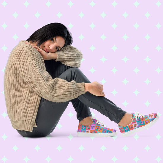 A person sits on the floor, leaning their head on one arm, wearing a beige sweater, dark pants, and My Favourite Colour is Rainbows Crazi Corgis Canvas Sneakers. Shown on a pastel background.