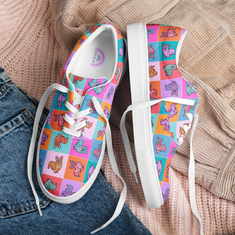 The Crazi Corgis Canvas Sneakers by My Favourite Colour is Rainbow are vibrant women's lace-up canvas shoes. Featuring a playful corgi pattern in vivid colours against a pink, purple, blue, and orange background, they are placed on a flat lay of jeans and a beige knit sweater.