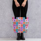 A person in black pants and boots holds a trendy Crazi Corgis Tote Bag by My Favourite Colour is Rainbow, boasting ample space with a pop art corgi pattern on a checkerboard of pink, turquoise, orange, and purple squares.