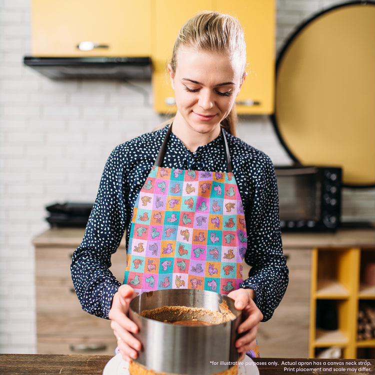 In a kitchen featuring yellow cabinets and a brick backsplash, a woman wearing a Crazi Corgis Apron by My Favourite Colour is Rainbow stands focused on her task, holding a cake tin. Her stylish navy polka dot shirt complements the vibrant setting.