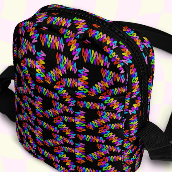 Introducing the Electric Zigzag Mini Crossbody Bag by My Favourite Colour is Rainbow, featuring a sleek black background and vibrant hues of pink, blue, green, yellow, and orange. Designed with adjustable straps for comfort, its perfect for those who love bold style and functionality.