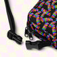 Close-up of My Favourite Colour is Rainbows Electric Zigzag Mini Crossbody Bag, featuring adjustable black straps, two buckles, and top zippers. The bag displays an Electric Zigzag print on a black background against a soft pastel checkerboard backdrop.