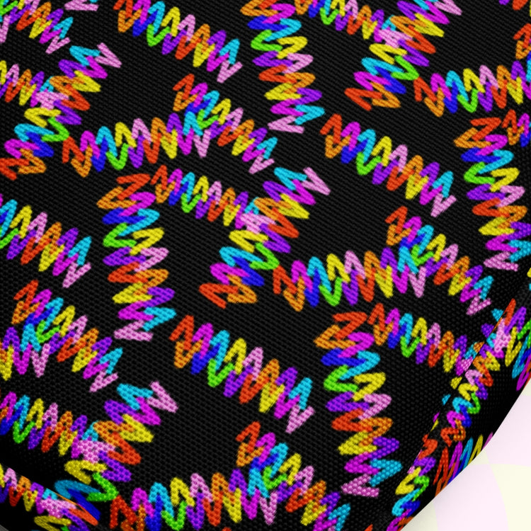 A close-up of the Electric Zigzag Mini Crossbody Bag by My Favourite Colour is Rainbow displays its vibrant black design with neon pink, blue, orange, green, and yellow hues. The adjustable straps enhance its dynamic style and functionality.