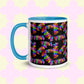 The My Favourite Colour is Rainbow Electric Zigzag Mug features a ceramic build with a blue handle and rim, showcasing colorful zigzag lines on a black background, set against a pale yellow backdrop with a pink floral pattern. Ideal for enhancing your coffee break.