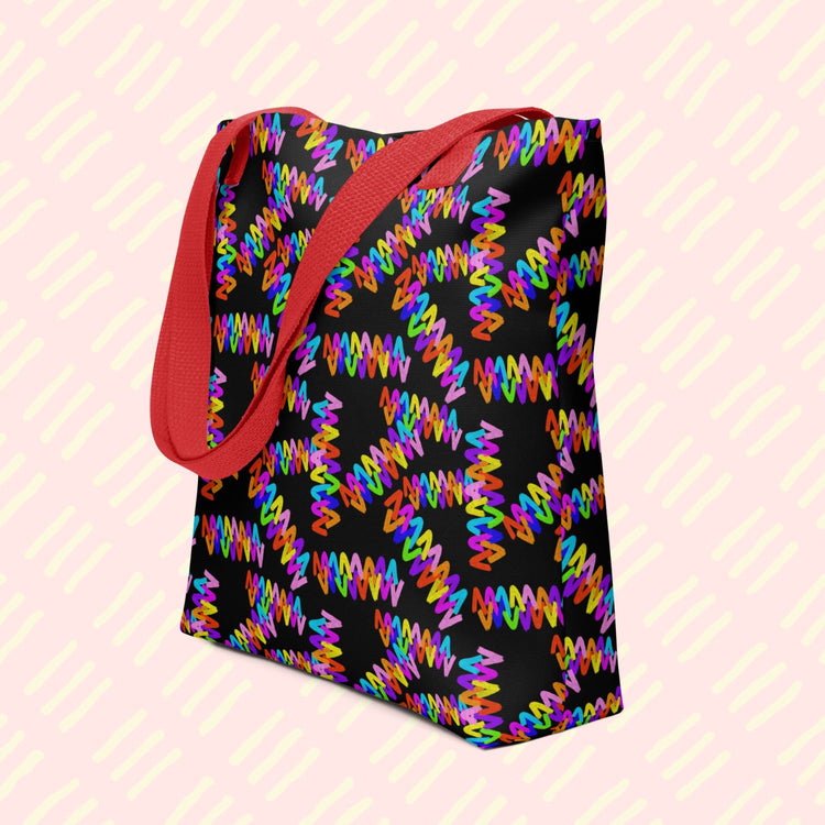 The Electric Zigzag Tote Bag by My Favourite Colour is Rainbow featuring a vibrant zigzag pattern in bright rainbow colours: red, orange, yellow, green, blue, purple and pink.  This version has a red handle.