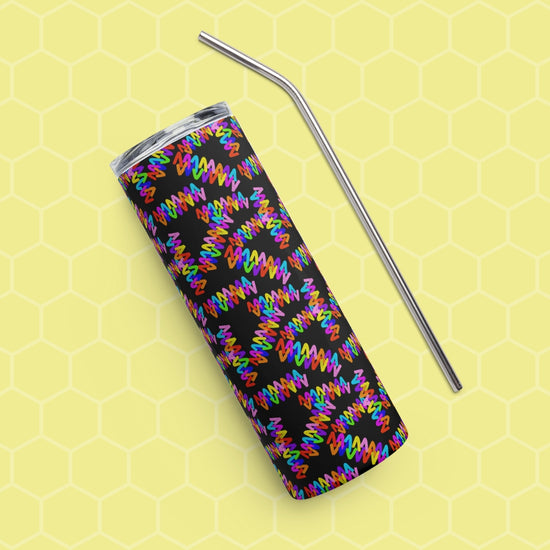 The Electric Zigzag Stainless Steel Tumbler by My Favourite Colour is Rainbow, featuring rainbow squiggles, rests on a yellow hexagonal-patterned surface with a metal straw beside it. The vibrant design contrasts strikingly against the muted background.