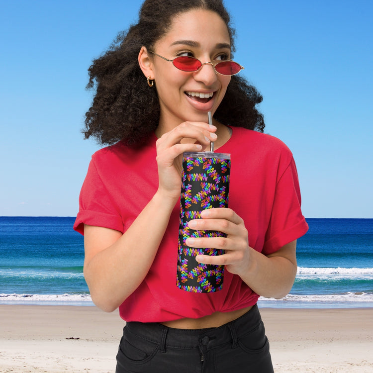 A woman in a red shirt and matching sunglasses stands on the beach, sipping from My Favourite Colour is Rainbows Electric Zigzag Stainless Steel Tumbler with a metal straw. The ocean and sky provide a perfect backdrop for this eco-friendly moment.