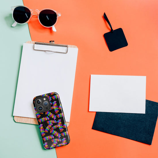 A clipboard with a blank sheet, trendy sunglasses, and a smartphone featuring the vibrant Electric Zigzag MagSafe iPhone Case from My Favourite Colour is Rainbow rest elegantly on a split green and orange background. Accompanied by two blank cards, it showcases style and functionality in harmony.