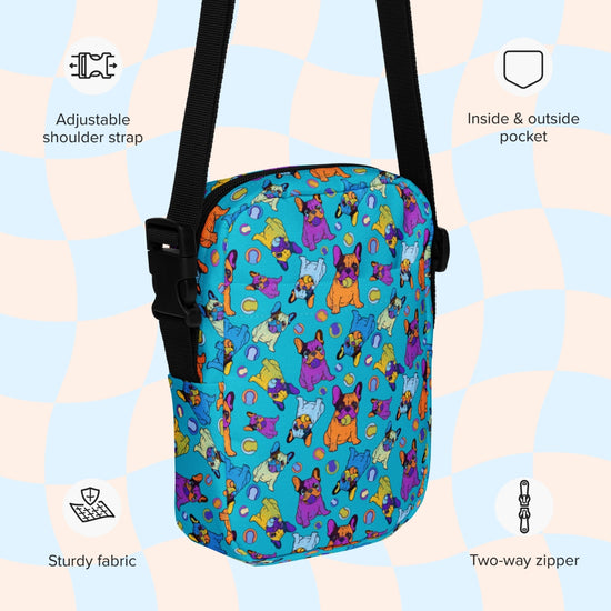 The Frenchie Fetch, Set, Match Mini Crossbody bag by My Favourite Colour is Rainbow features a vibrant cat pattern on blue fabric. It has adjustable straps, inside and outside pockets, sturdy construction, a two-way zipper, and icons/text highlighting its water resistance on a checkered background.