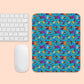 The Frenchie Fetch, Set, Match Mouse Pad by My Favourite Colour is Rainbow displays a playful design with cartoon animals and shapes in orange, blue, purple, and teal. Its placed beside a white keyboard and mouse on a light peach surface.