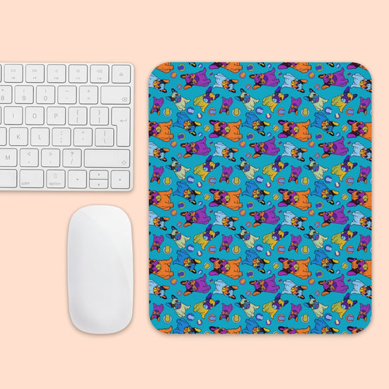 The Frenchie Fetch, Set, Match Mouse Pad by My Favourite Colour is Rainbow displays a playful design with cartoon animals and shapes in orange, blue, purple, and teal. Its placed beside a white keyboard and mouse on a light peach surface.