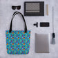 A flat lay features the spacious and trendy Frenchie Fetch, Set, Match Tote Bag by My Favourite Colour is Rainbow with a colourful cartoon french bulldog and tennis ball design, alongside a notebook, sunglasses, three pens, smartphone, clip-on camera lens, laptop, and tassel keychain on a speckled surface.