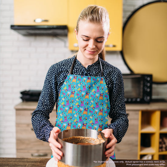 A woman with light hair tied back wears the Frenchie Fetch, Set, Match Apron by My Favourite Colour is Rainbow. She holds a baking tin with a crust base while her lively apron perfectly complements the rooms yellow cabinet and brick backsplash.