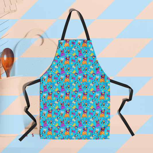 The Frenchie Fetch, Set, Match Apron by My Favourite Colour is Rainbow showcases cartoon bulldogs and tennis balls on a vibrant blue background. In the background are  a white container with wooden spoons and a cutting board.