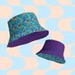 Two bucket hats are displayed as streetwear accessories. The Frenchie Fetch, Set, Match Reversible Bucket Hat by My Favourite Colour is Rainbow features a blue base with colorful cartoon animals and a reversible purple exterior with the same pattern. A retro blue and peach geometric design decorates the background.