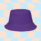 The Frenchie Fetch, Set, Match Reversible Bucket Hat by My Favourite Colour is Rainbow stands out in purple against light blue and beige curves, making it the perfect streetwear accessory.