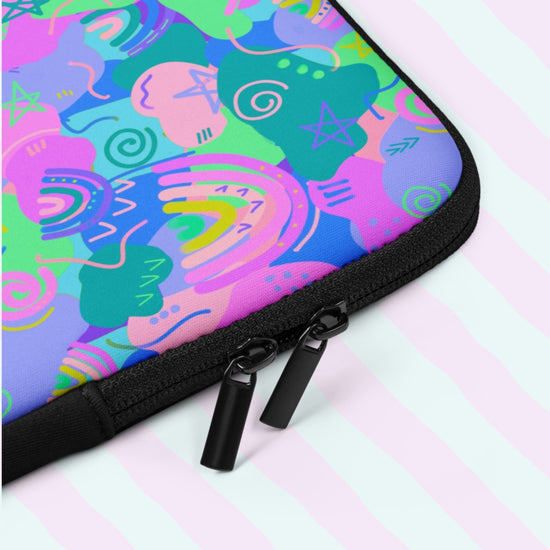 A close up of the Funfetti Laptop Sleeve by My Favourite Colour is Rainbow,  featuring playful pink, blue, and green abstract shapes with doodles like rainbows, stars and spirals. It includes a black zipper with dual pulls.  The print is on only one side of the laptop sleeve, the other side is black.