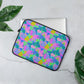 The 13" Funfetti Laptop Sleeve by My Favourite Colour is Rainbow, with a vibrant design of pink, green, blue, and purple rainbows, stars, swirls and abstract shapes, has a silver laptop coming out of it.  It is displayed on a light gray surface, bordered by large green leaves.  The print is on only one side of the laptop sleeve, the other side is black.