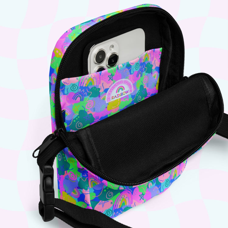 The Funfetti Mini Crossbody Bag by My Favourite Colour is Rainbow features a vibrant Funfetti print with a small rainbow emblem, a black strap, and an open front pocket perfect for holding your smartphone, all set against a subtle checkered pastel background.