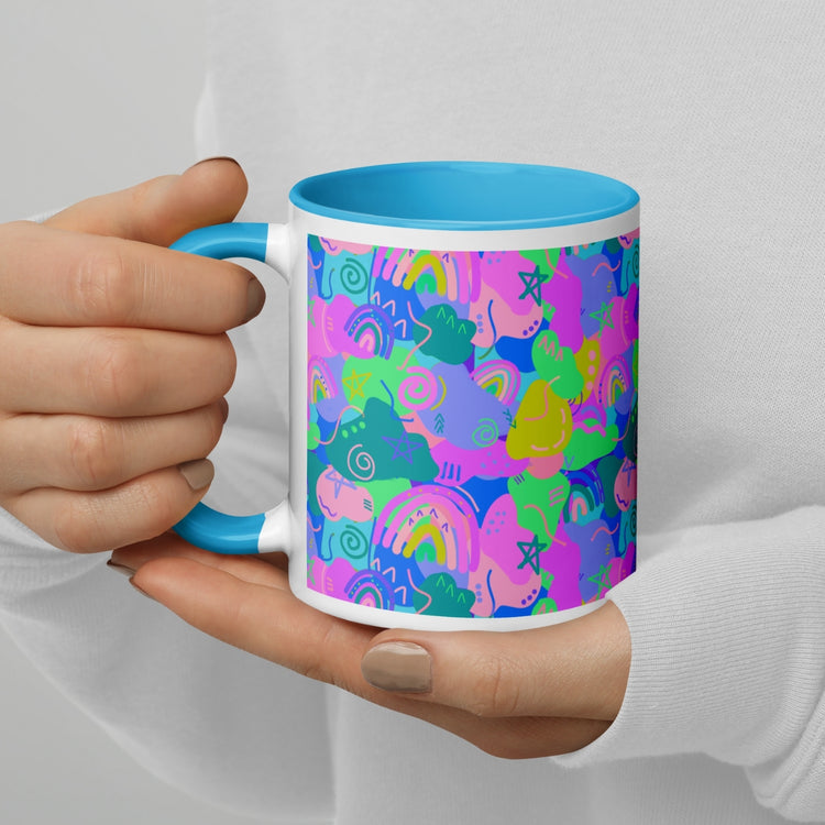 An individual in a white shirt holds the My Favourite Colour is Rainbows Funfetti Mug, showcasing its vibrant blue, green, pink, and purple abstract patterns. The ceramic mugs blue handle and interior beautifully contrast with its lively exterior design.