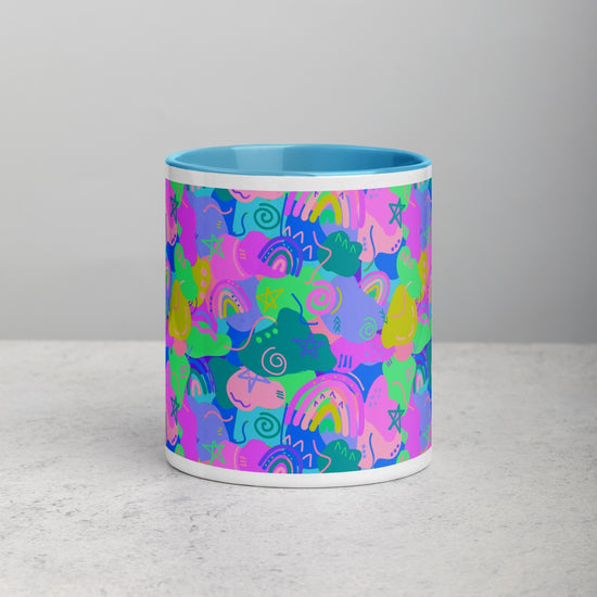 The Funfetti Mug by My Favourite Colour is Rainbow features a vibrant ceramic design with an abstract pattern in blue, pink, green, and purple. Shapes resemble rainbows, spirals, and stars. The interior is light blue and it rests on a light gray surface.
.