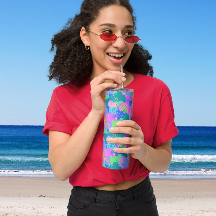 A woman in a red shirt and matching sunglasses enjoys her iced coffee from a Funfetti Stainless Steel Tumbler by My Favourite Colour is Rainbow while standing on the beach, with ocean waves rolling in under the clear blue sky.