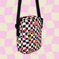 The Galaxy Mini Crossbody Bag by My Favourite Colour is Rainbow features a black and white checkered pattern with gold, pink and red rainbows, stars, and hearts. It is made of canvas-type material, has internal and external pockets and a black strap with a buckle on one side that can be extended to crossbody length.
