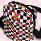 The Galaxy Mini Crossbody Bag by My Favourite Colour is Rainbow features a black and white checkered pattern with glittery gold, pink and red rainbows, stars, and hearts.  It is made of canvas-type material, has internal and external pockets and a black strap with a buckle on one side that can be extended to crossbody length.
