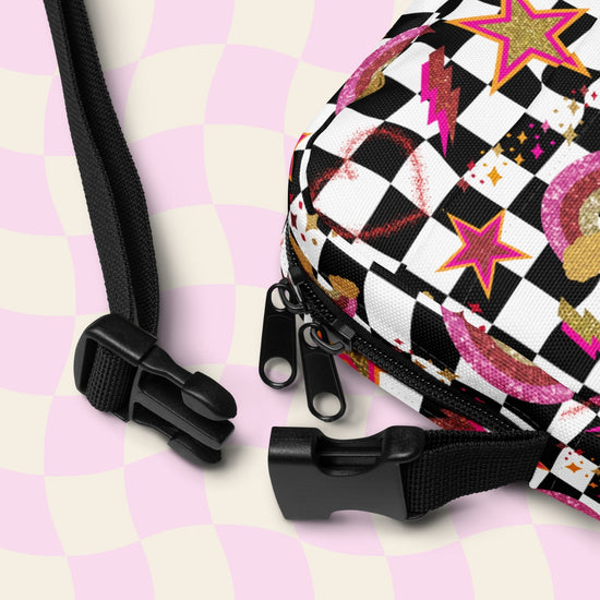 The Galaxy Mini Crossbody Bag by My Favourite Colour is Rainbow features a colourful checkered design with stars, lightning bolts, and circles. It has black zippers and adjustable straps for comfort.