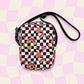 The Galaxy Mini Crossbody Bag by My Favourite Colour is Rainbow is a compact, durable crossbody featuring a black and white checkered pattern with glittery gold, pink and red rainbows, stars, and hearts. It is made of canvas-type material, has internal and external pockets and a black strap with a buckle on one side that can be extended to crossbody length.
